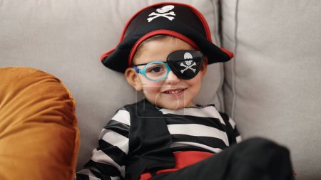 Foto de Adorable niño hispano con traje de pirata sentado en el sofá en casa - Imagen libre de derechos