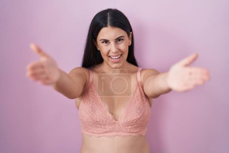 Foto de Mujer hispana joven con sostén rosa mirando a la cámara sonriendo con los brazos abiertos para abrazarse. expresión alegre abrazando la felicidad. - Imagen libre de derechos
