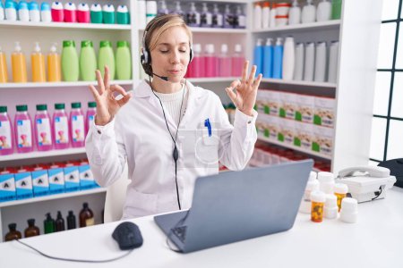 Photo for Young caucasian woman working at pharmacy drugstore using laptop relax and smiling with eyes closed doing meditation gesture with fingers. yoga concept. - Royalty Free Image