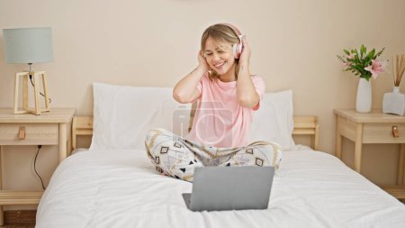Foto de Mujer rubia joven escuchando música bailando en la cama en el dormitorio - Imagen libre de derechos