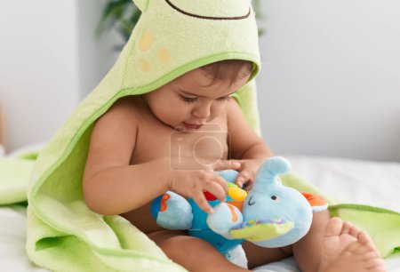 Photo for Adorable hispanic baby wearing frog towel playing with elephant toy at bedroom - Royalty Free Image