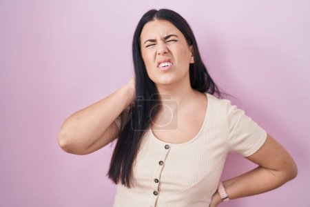 Foto de Young hispanic woman standing over pink background suffering of neck ache injury, touching neck with hand, muscular pain - Imagen libre de derechos
