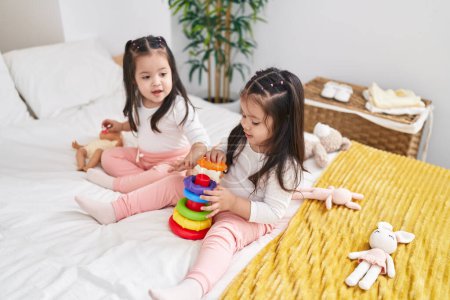 Téléchargez les photos : Adorables filles jumelles jouant avec cerceaux jeu assis sur le lit dans la chambre - en image libre de droit