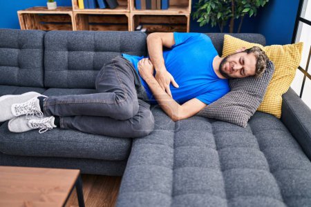 Foto de Joven que sufre de dolor de estómago tumbado en el sofá en casa - Imagen libre de derechos
