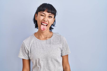 Photo for Young hispanic woman wearing casual t shirt over blue background sticking tongue out happy with funny expression. emotion concept. - Royalty Free Image