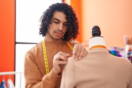 Foto de Joven hombre latino sastrería chaqueta de costura de pie por maniquí en atelier - Imagen libre de derechos