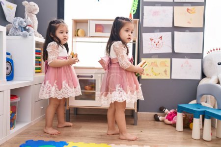 Foto de Adorables chicas gemelas jugando con la cocina de juego de pie en el jardín de infantes - Imagen libre de derechos