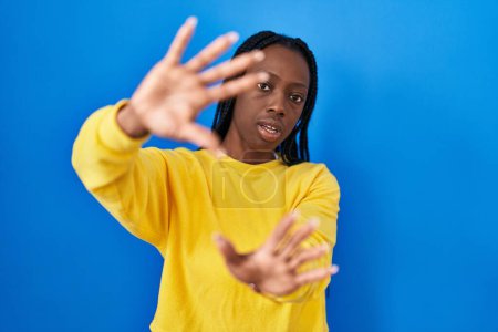Photo for Beautiful black woman standing over blue background doing frame using hands palms and fingers, camera perspective - Royalty Free Image