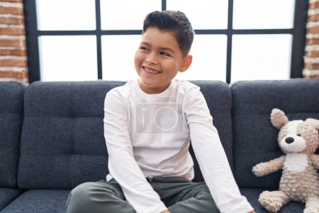 Téléchargez les photos : Adorable garçon hispanique souriant confiant assis sur le canapé à la maison - en image libre de droit