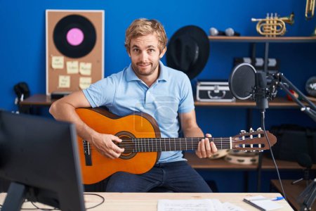 Téléchargez les photos : Homme caucasien jouant de la guitare classique au studio de musique expression désemparée et confuse. concept de doute. - en image libre de droit