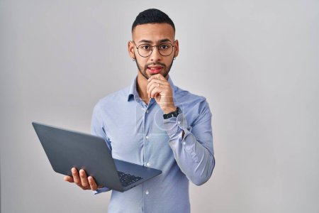 Photo for Young hispanic man working using computer laptop thinking worried about a question, concerned and nervous with hand on chin - Royalty Free Image
