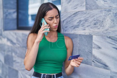 Téléchargez les photos : Jeune belle femme hispanique parlant sur smartphone tenant la carte de crédit à la rue - en image libre de droit