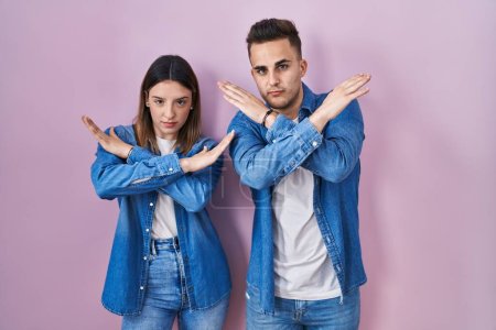 Téléchargez les photos : Jeune couple hispanique debout sur fond rose expression de rejet croisant les bras faisant signe négatif, visage en colère - en image libre de droit