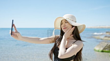 Téléchargez les photos : Jeune femme chinoise touriste portant maillot de bain faire selfie par smartphone au bord de la mer - en image libre de droit