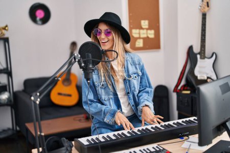 Foto de Young woman musician singing song playing piano keyboard at music studio - Imagen libre de derechos