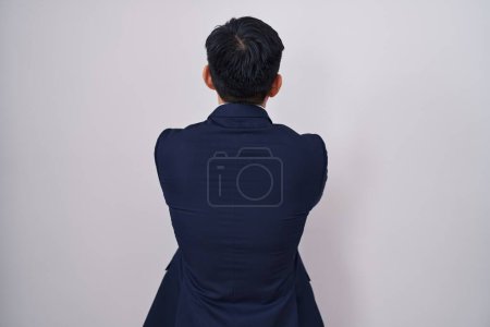 Téléchargez les photos : Jeune homme asiatique portant costume d'affaires et cravate debout vers l'arrière regardant loin avec les bras croisés - en image libre de droit