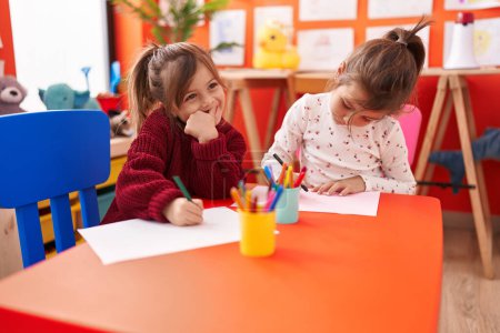 Foto de Adorables estudiantes de preescolar niñas sentados en el dibujo de la mesa en papel en el jardín de infantes - Imagen libre de derechos