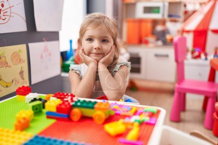 Photo for Adorable blonde girl playing with construction blocks sitting on table at kindergarten - Royalty Free Image