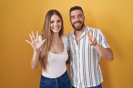 Photo for Young couple standing over yellow background showing and pointing up with fingers number seven while smiling confident and happy. - Royalty Free Image