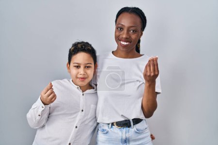 Téléchargez les photos : Jeune mère et son fils debout ensemble sur fond blanc faisant geste d'argent avec les mains, demandant le paiement du salaire, entreprise millionnaire - en image libre de droit