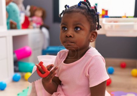 Foto de Afro-americana chica sentado en piso holding herramienta en kindergarten - Imagen libre de derechos