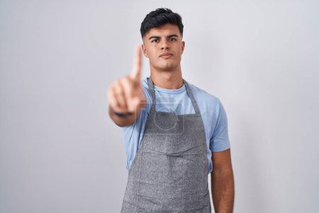 Photo for Hispanic young man wearing apron over white background pointing with finger up and angry expression, showing no gesture - Royalty Free Image
