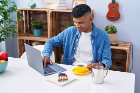 Foto de Joven latino usando laptop desayunando en casa - Imagen libre de derechos