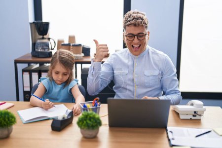 Photo for Young father and daughter working at the office together pointing thumb up to the side smiling happy with open mouth - Royalty Free Image