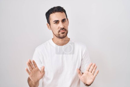 Photo for Handsome hispanic man standing over white background moving away hands palms showing refusal and denial with afraid and disgusting expression. stop and forbidden. - Royalty Free Image