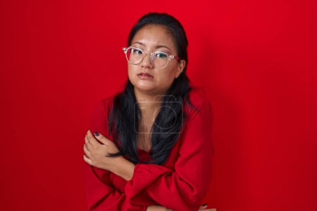Photo for Asian young woman standing over red background shaking and freezing for winter cold with sad and shock expression on face - Royalty Free Image