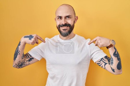 Photo for Young hispanic man with tattoos standing over yellow background looking confident with smile on face, pointing oneself with fingers proud and happy. - Royalty Free Image