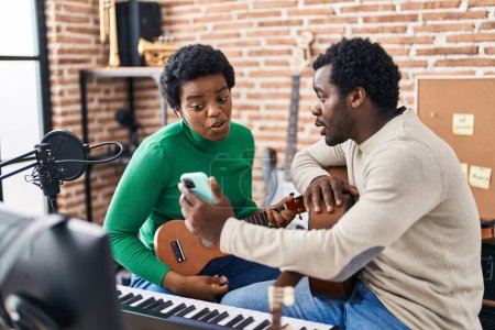 Foto de Africano americano hombre y mujer grupo de música usando teléfono inteligente jugando ukelele en estudio de música - Imagen libre de derechos