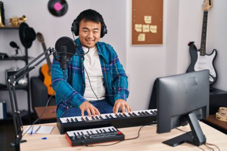 Foto de Young chinese man singer singing song playing piano keyboard at music studio - Imagen libre de derechos
