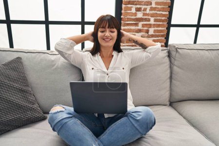 Photo for Young beautiful hispanic woman using laptop relaxed on sofa at home - Royalty Free Image