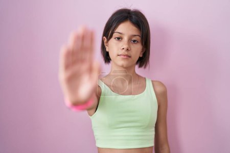 Photo for Young girl standing over pink background doing stop sing with palm of the hand. warning expression with negative and serious gesture on the face. - Royalty Free Image