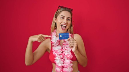 Foto de Joven turista rubia señalando a la tarjeta de crédito sonriendo sobre fondo rojo aislado - Imagen libre de derechos