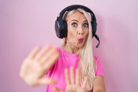 Photo for Caucasian woman listening to music using headphones afraid and terrified with fear expression stop gesture with hands, shouting in shock. panic concept. - Royalty Free Image