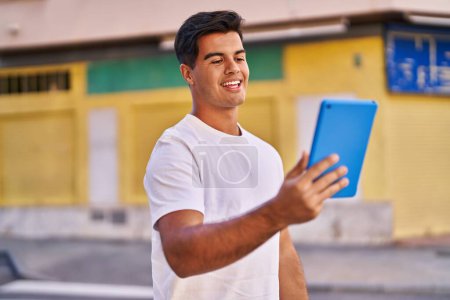 Téléchargez les photos : Jeune homme hispanique souriant confiant en utilisant touchpad à la rue - en image libre de droit