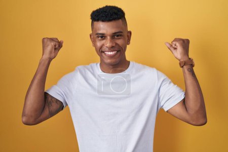 Téléchargez les photos : Jeune homme hispanique debout sur fond jaune célébrant surpris et étonnés pour le succès avec les bras levés et les yeux fermés. concept gagnant. - en image libre de droit
