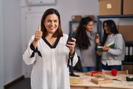 Téléchargez les photos : Trois femmes travaillant dans le commerce électronique des petites entreprises souriant heureux et positif, pouce levé faire excellent et signe d'approbation - en image libre de droit