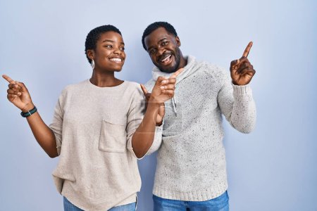 Téléchargez les photos : Jeune couple afro-américain debout sur fond bleu ensemble souriant confiant pointant avec les doigts vers différentes directions. espace de copie pour la publicité - en image libre de droit