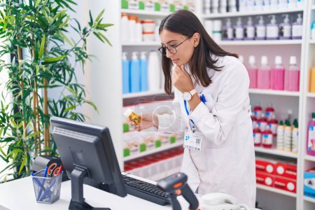 Photo for Young beautiful hispanic woman pharmacist using computer holding pills bottle at pharmacy - Royalty Free Image