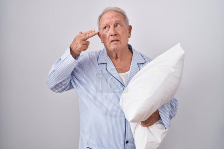Photo for Senior man with grey hair wearing pijama hugging pillow shooting and killing oneself pointing hand and fingers to head like gun, suicide gesture. - Royalty Free Image