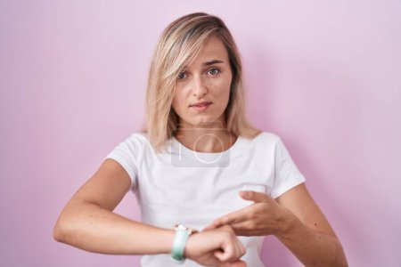 Téléchargez les photos : Young blonde woman standing over pink background in hurry pointing to watch time, impatience, upset and angry for deadline delay - en image libre de droit