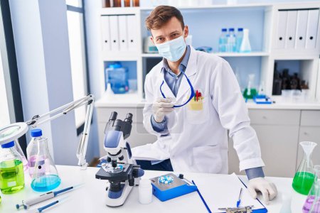 Foto de Joven científico con máscara médica sentado en la mesa en el laboratorio - Imagen libre de derechos