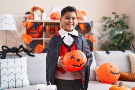 Foto de Adorable niño hispano con disfraz de halloween sosteniendo canasta de calabaza en casa - Imagen libre de derechos