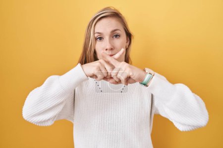 Foto de Mujer joven caucásica usando suéter blanco sobre fondo amarillo expresión rechazo cruzando dedos haciendo signo negativo - Imagen libre de derechos