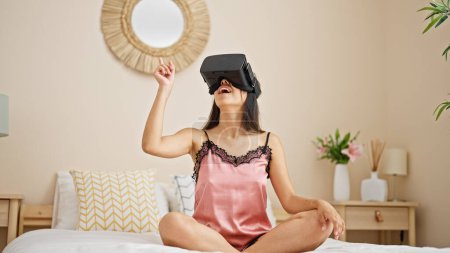 Téléchargez les photos : Jeune belle femme hispanique jouant à un jeu vidéo en utilisant des lunettes de réalité virtuelle dans la chambre - en image libre de droit