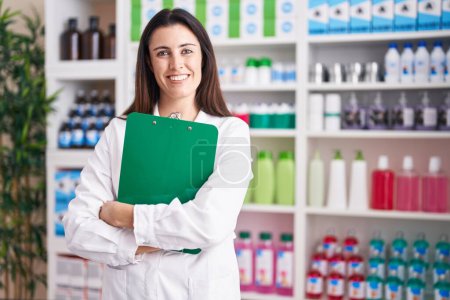 Photo for Young beautiful hispanic woman pharmacist smiling confident holding clipboard at pharmacy - Royalty Free Image