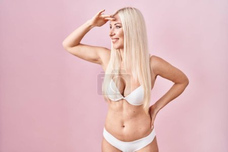 Photo for Caucasian woman wearing lingerie over pink background very happy and smiling looking far away with hand over head. searching concept. - Royalty Free Image